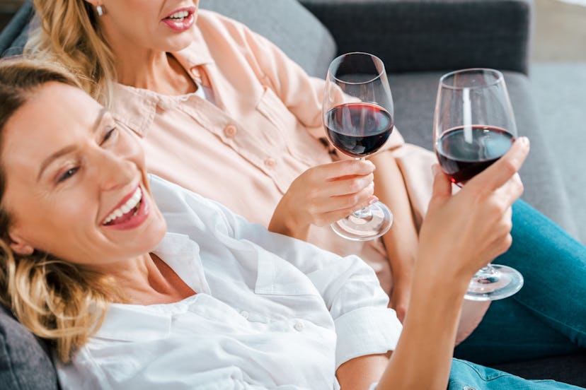 cropped shot of mature mother and adult daughter with glasses of red wine spending time together at ...