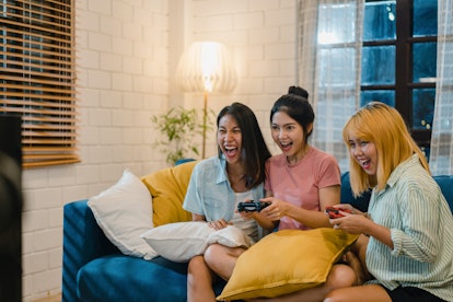 Group of Asian women couple play games at home, female using joystick having funny moment together o...
