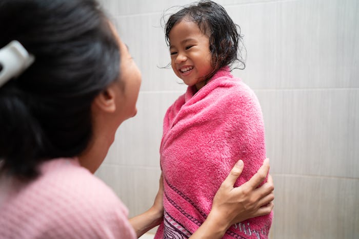 happy young kid being dry by her mom using towel after taking shower in the bathroom