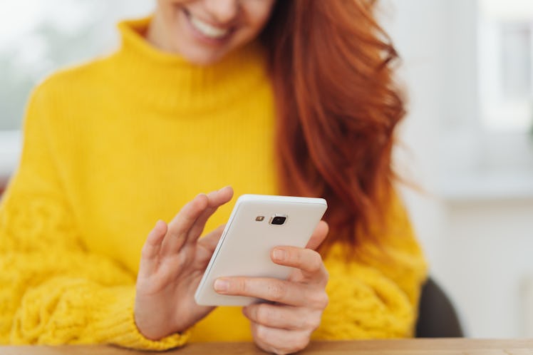 Lower face and body of your red haired woman in yellow sweater texting on mobile.