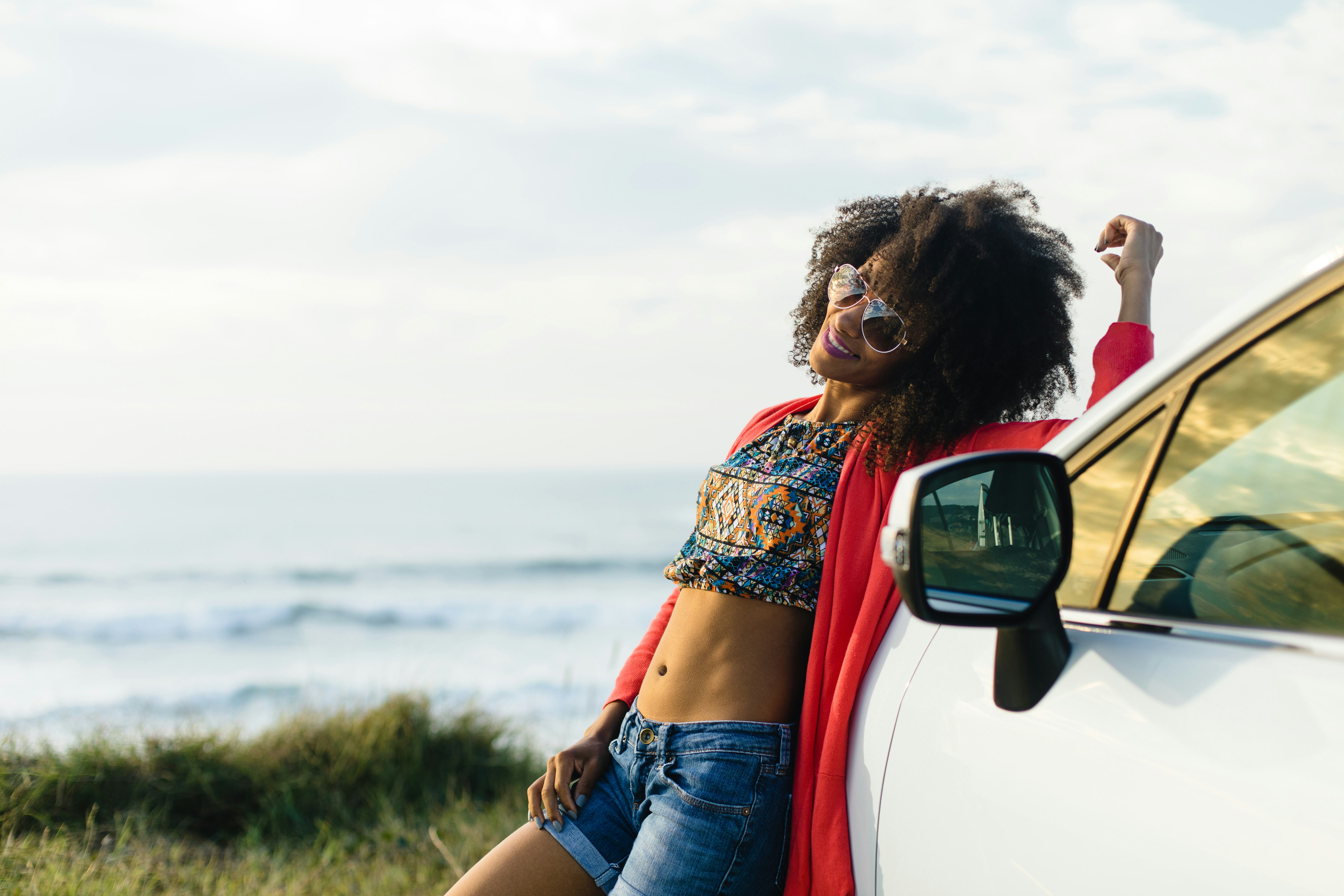 Happy stylish black woman relaxing on a car trip to the coast. Fashionable afro hair model on vacati...