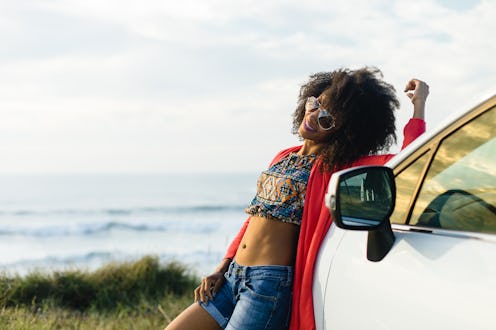 Happy stylish black woman relaxing on a car trip to the coast. Fashionable afro hair model on vacati...