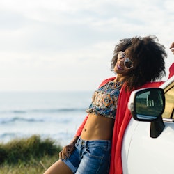 Happy stylish black woman relaxing on a car trip to the coast. Fashionable afro hair model on vacati...