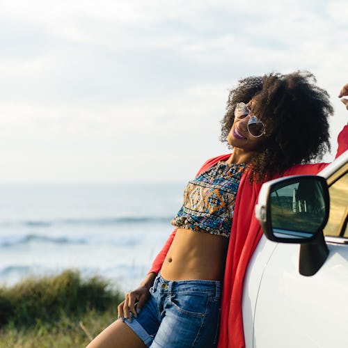 Happy stylish black woman relaxing on a car trip to the coast. Fashionable afro hair model on vacati...