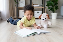 Adorable toddler mixed race boy reading book at home or in kindergarten, beautiful preschooler child...
