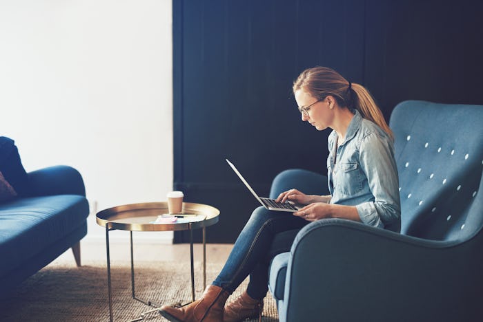 Smiling young businesswoman browsing online with a laptop while sitting on a sofa in a modern office