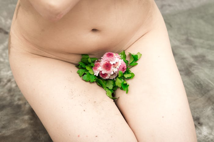 Caption of nude woman crotch sitting on her knees with plant and flower covering vagina