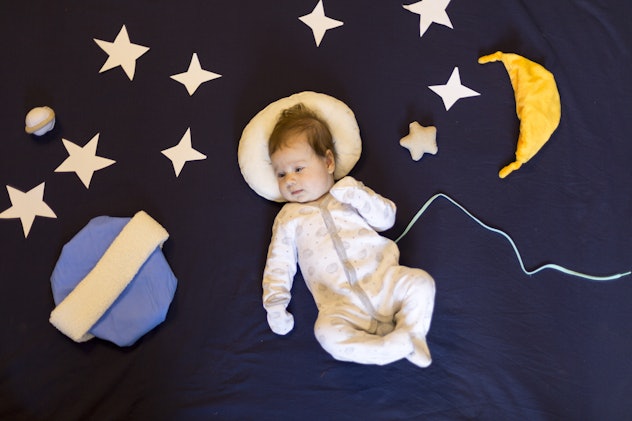Little baby girl flying in space in spacesuit among stars and planets and the moon