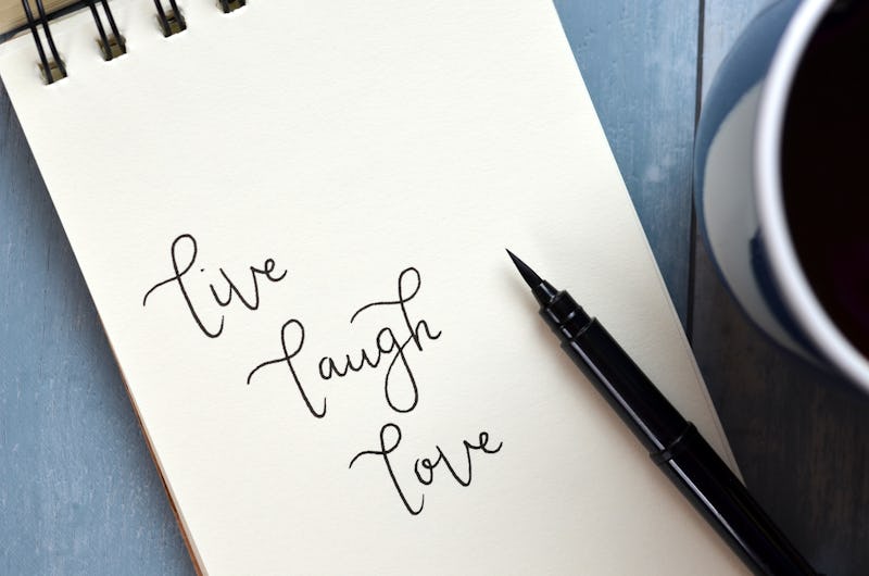 LIVE LAUGH LOVE written in notepad on blue wooden background with cup of coffee and pen