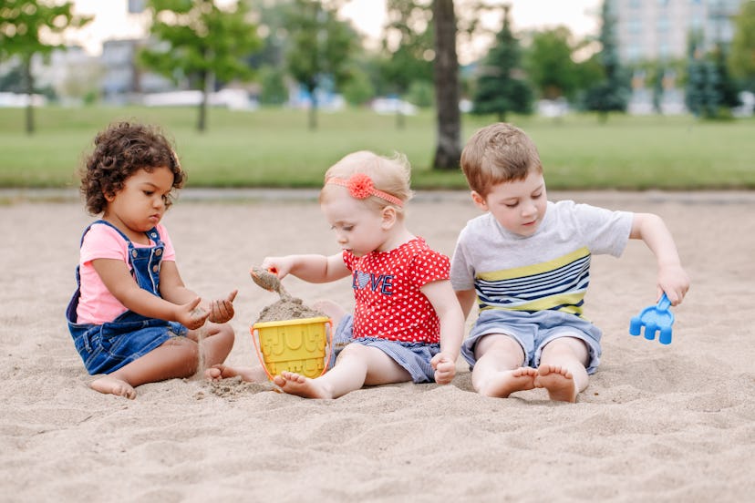 Portrait of three cute Caucasian and hispanic latin toddlers babies children sitting in sandbox play...