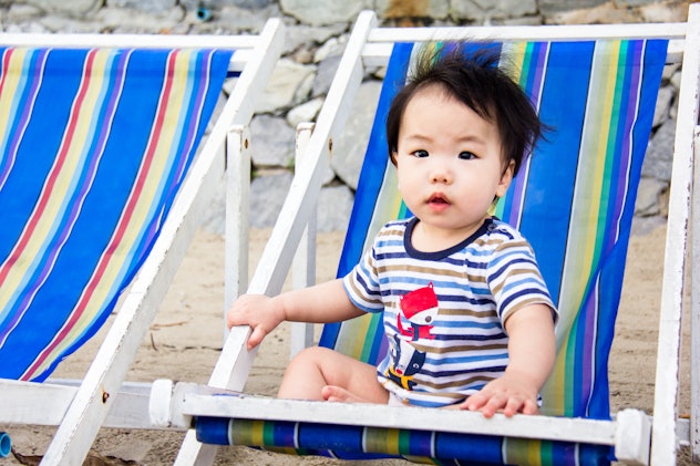 A little baby is enjoy sitting on the colorful beach chair at the seacoast. Grey stone wall backgrou...