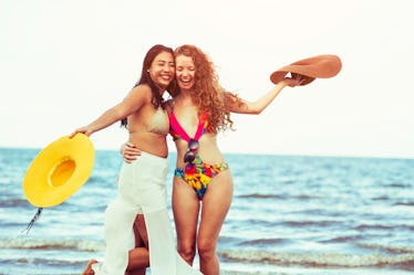 Happy women in bikinis dance together on tropical sand beach in summer vacation. Travel lifestyle.