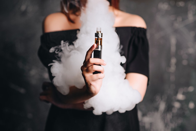 Close-up photo of female holding e-cigarette with smoke. Indoors