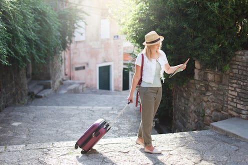 Girl traveler looks at city map with suitcase at town street in Europe. Woman tourist is searching a...