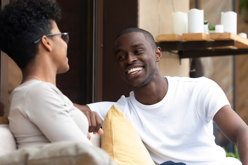 Happy african American millennial man and woman sit in coffee shop have fun talking or flirting, smi...