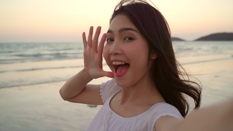 Tourist Asian woman selfie on beach, young beautiful female happy smiling using mobile phone taking ...