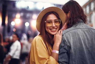Portrait of charming young lady in hat standing close to hipster guy and looking at camera with smil...