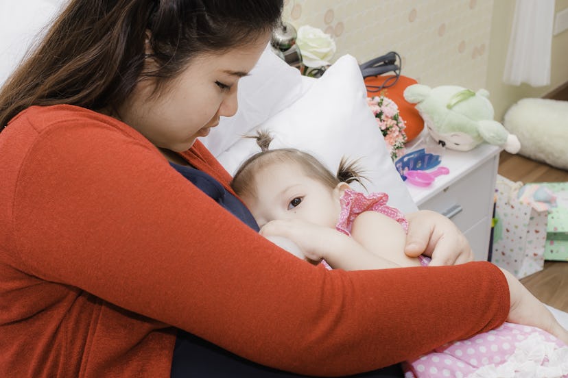 Young pregnant woman with red knitting sweater hugs her little cute baby on bed at home, when her ki...