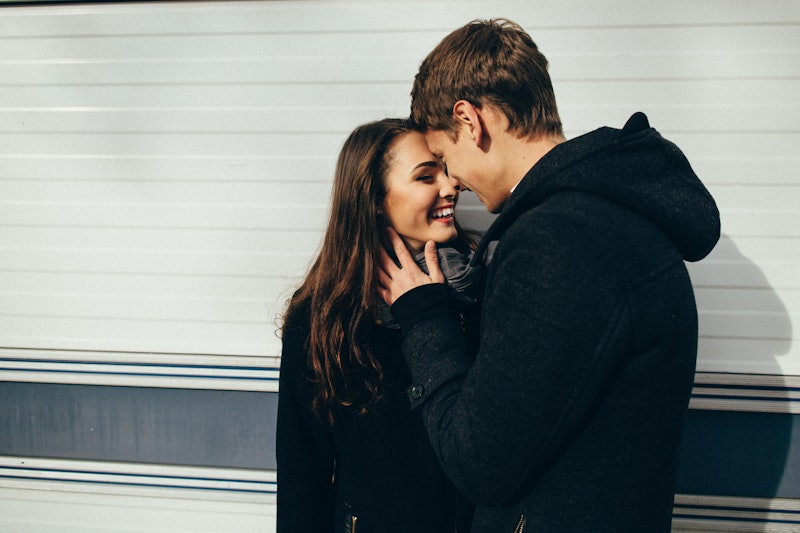 A couple wearing black jackets embraces and smiles outside on a sunny winter day.