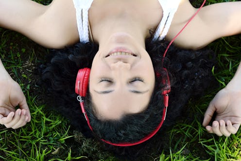 Portrait of young latin woman with headphones listening to music at the park in summer. Enjoying Mus...