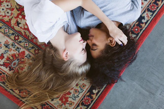 Young pretty woman with blond hair and nice african american woman with dark curly hair thoughtfully lying on vintage carpet spending time together at cozy home
