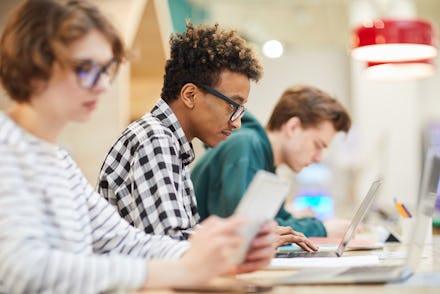 Busy students in computer class: serious concentrated young African-American student boy in glasses ...