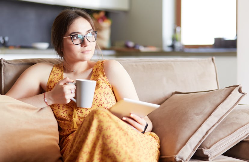 Young woman uses tablet while relaxing at home with coffee on the sofa couch