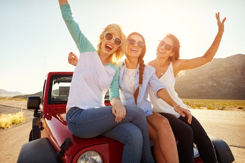 Three Female Friends On Road Trip Sit On Car Hood