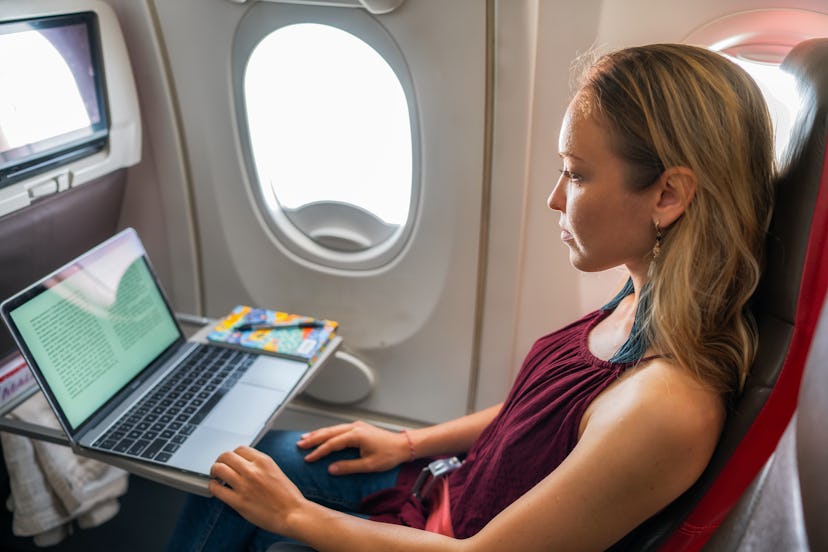 Young woman reading a book on laptop in plane