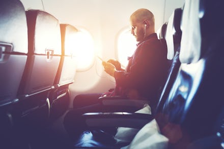 Man entrepreneur is watching video on mobile phone, while is sitting in plane near window with sun r...