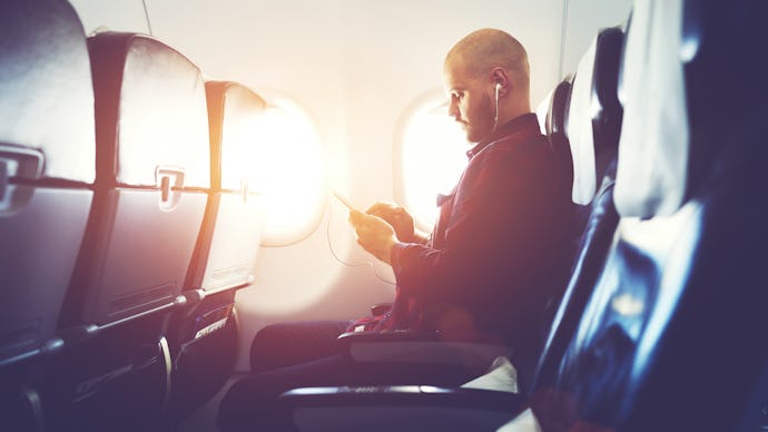 Man entrepreneur is watching video on mobile phone, while is sitting in plane near window with sun r...