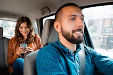 Smiling driver talking with female passenger. Woman using mobile phone in the background.