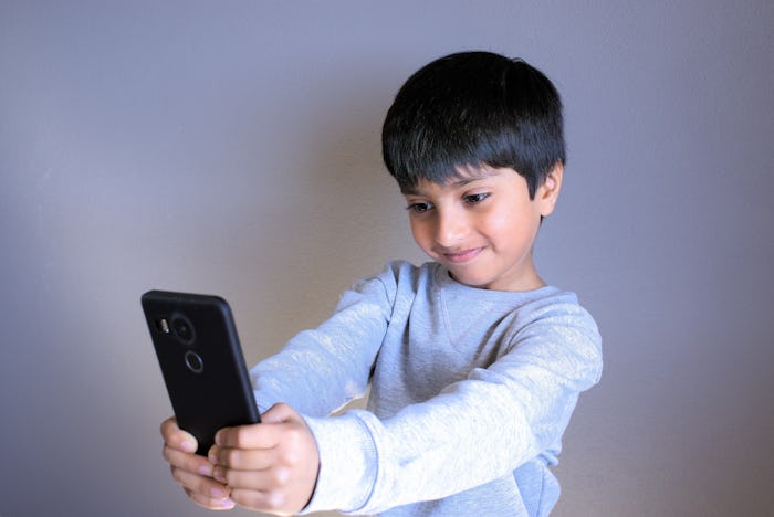 Kid looking at smartphone taking selfie. Indian Boy smiling taking photo of self. Kid taking selfie....