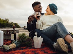 Man and woman toasting wine glasses at the picnic. Couple having wine on a romantic date outdoors.