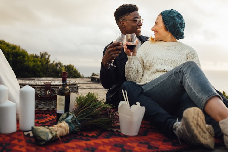 Man and woman toasting wine glasses at the picnic. Couple having wine on a romantic date outdoors.