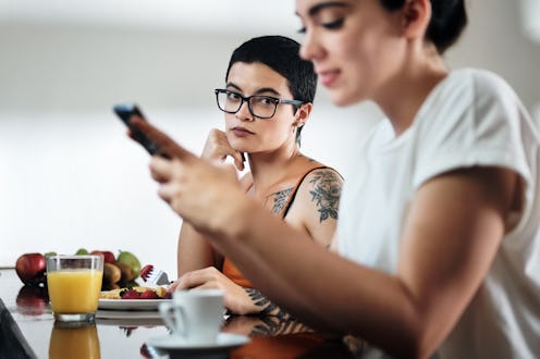 Domestic lifestyle with two lesbian women at home eating breakfast, partner chatting on mobile telep...