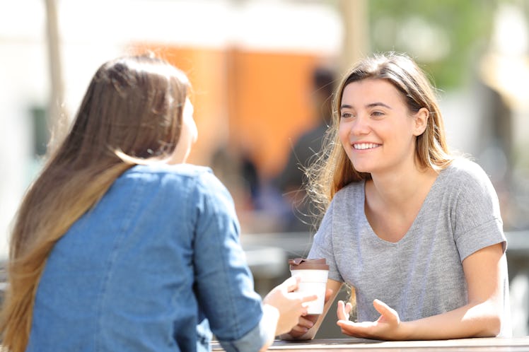 Two happy women talking sitting in a park a sunny day