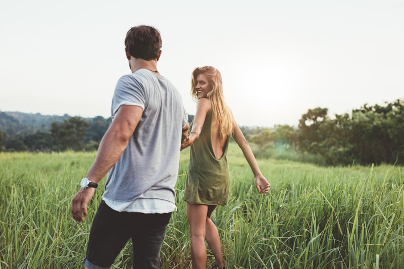 Rear view shot of young woman walking with her boyfriend on grass field. Couple enjoying a walk thro...