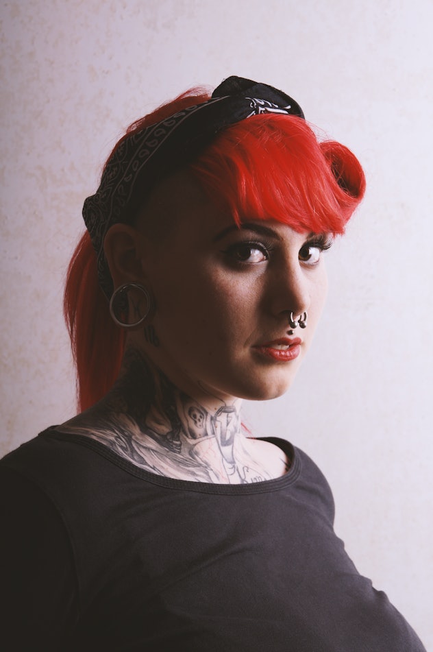 moody portrait with deep shadow of a young woman with many facial piercings and neck tattoos