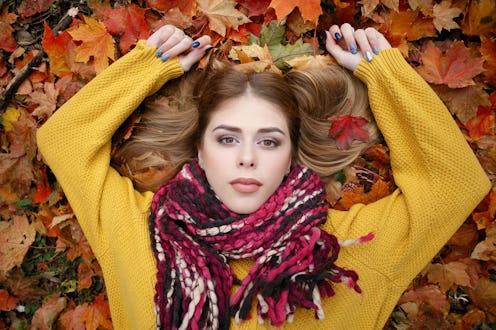 beauty, people, season and health concept - pretty girl is lying in yellow red Autumn leaves