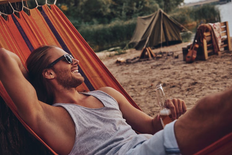 Real relaxation. Handsome young man keeping hand behind head and smiling while lying in hammock