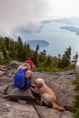 Adventurous Girl is hiking with a dog on top of Unnecessary Mountain during a sunny and cloudy summe...