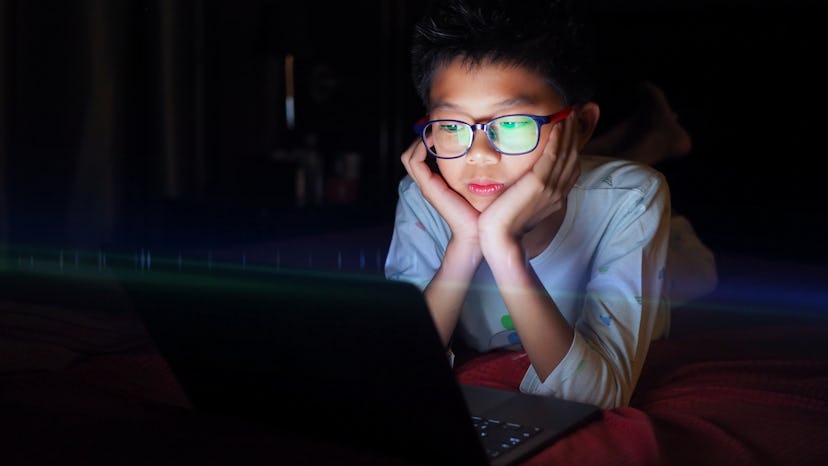 Asian boy lying in bed and watching laptop at night.