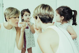 Beautiful mom showing how to use lipstick. Adorable girl looking at herself in mirror and imitating ...