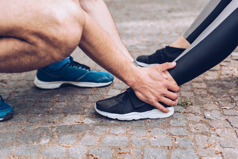 cropped shot of sportsman touching injured leg of sportswoman in sneakers