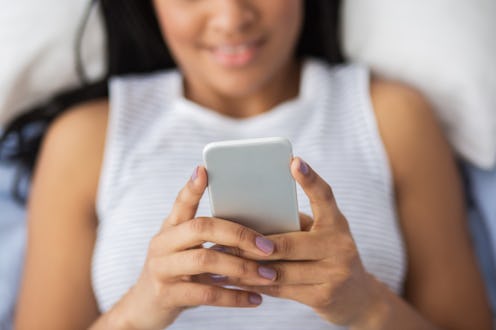 A woman reads from her phone in bed.