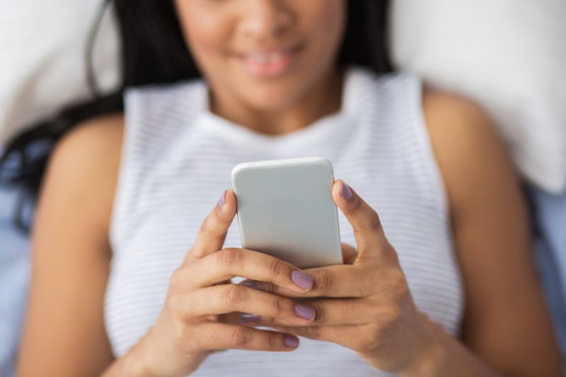 A woman reads from her phone in bed. 