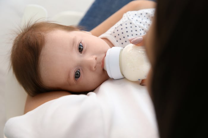 Woman feeding her baby from bottle at home, closeup