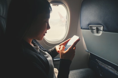 Tourist Asian woman sitting near airplane window and using Smart phone during flight.