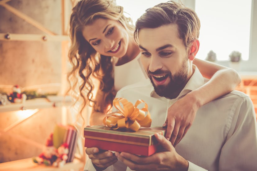 Beautiful young couple is celebrating at home. Pretty girl is giving her boyfriend a gift box